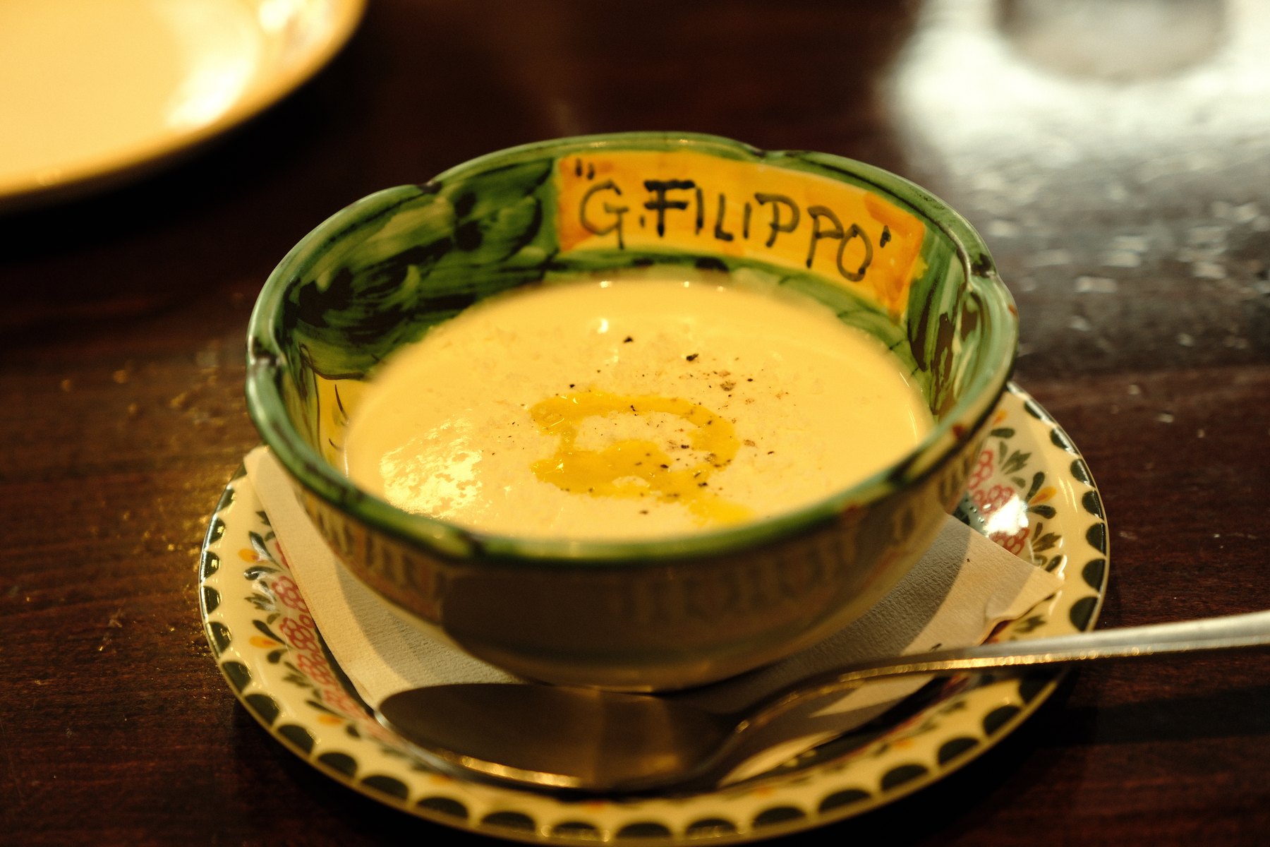 A ceramic bowl of pale soup on a dark wooden table under warm restaurant light