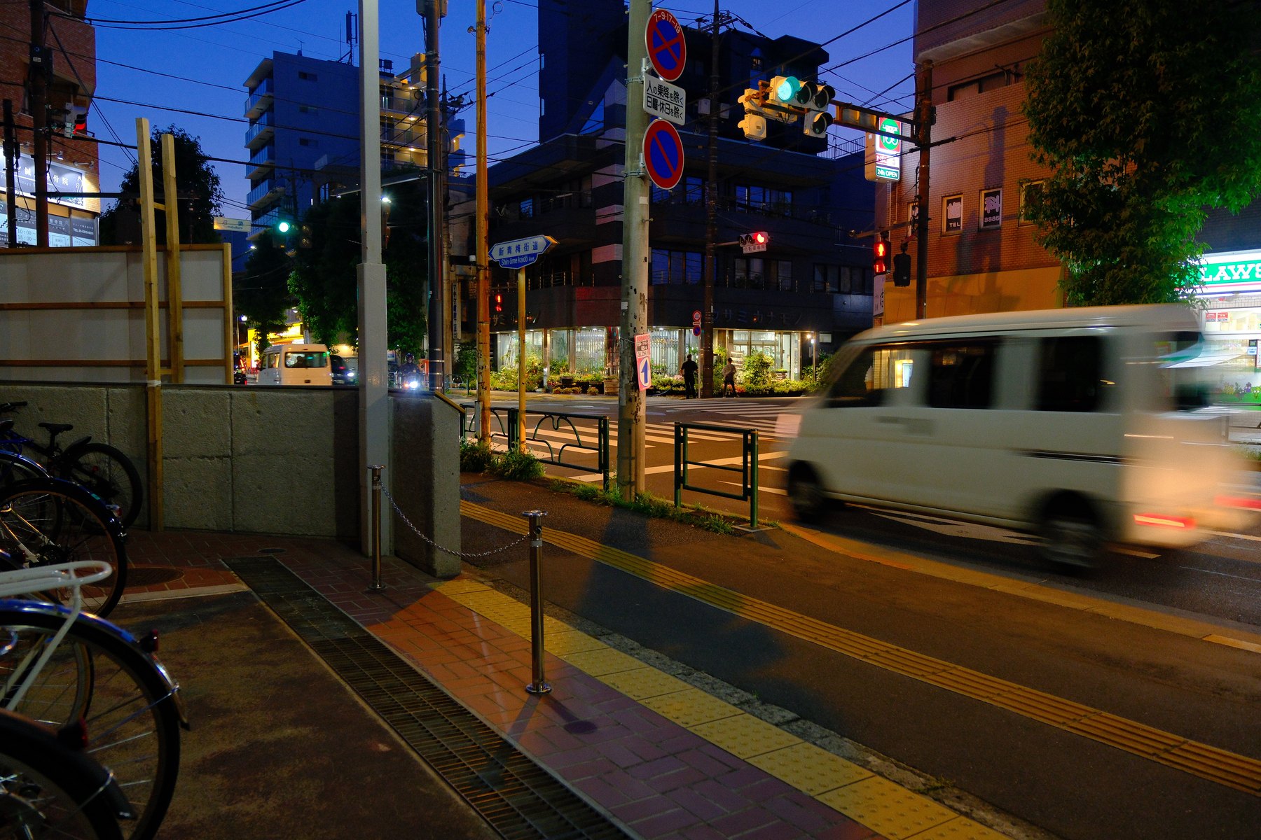 A white van moving through a Tokyo intersection at blue hour while the street and buildings remain sharp