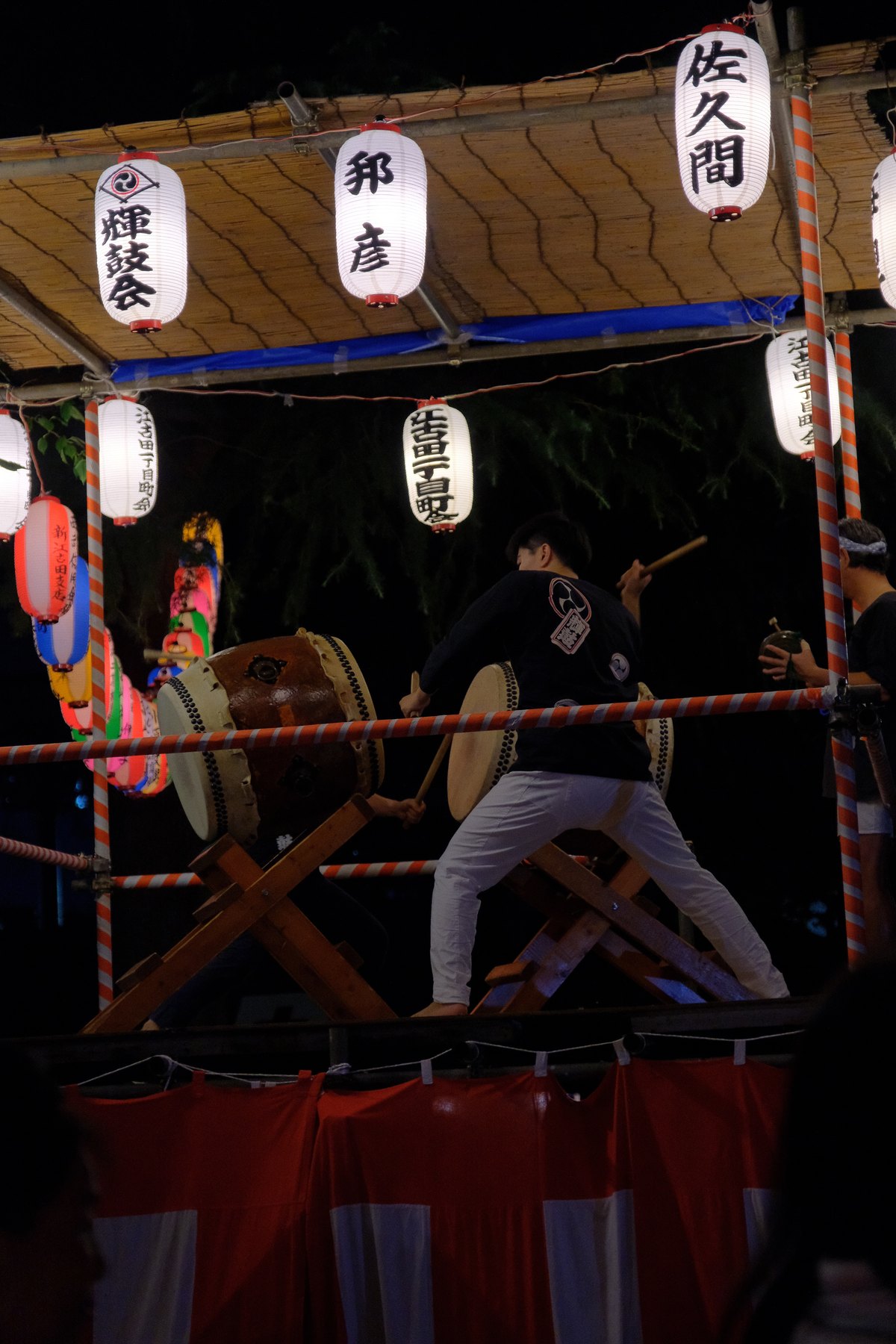 A Tokyo festival scene showing layered traditional clothing, lantern, rope, and drum colors