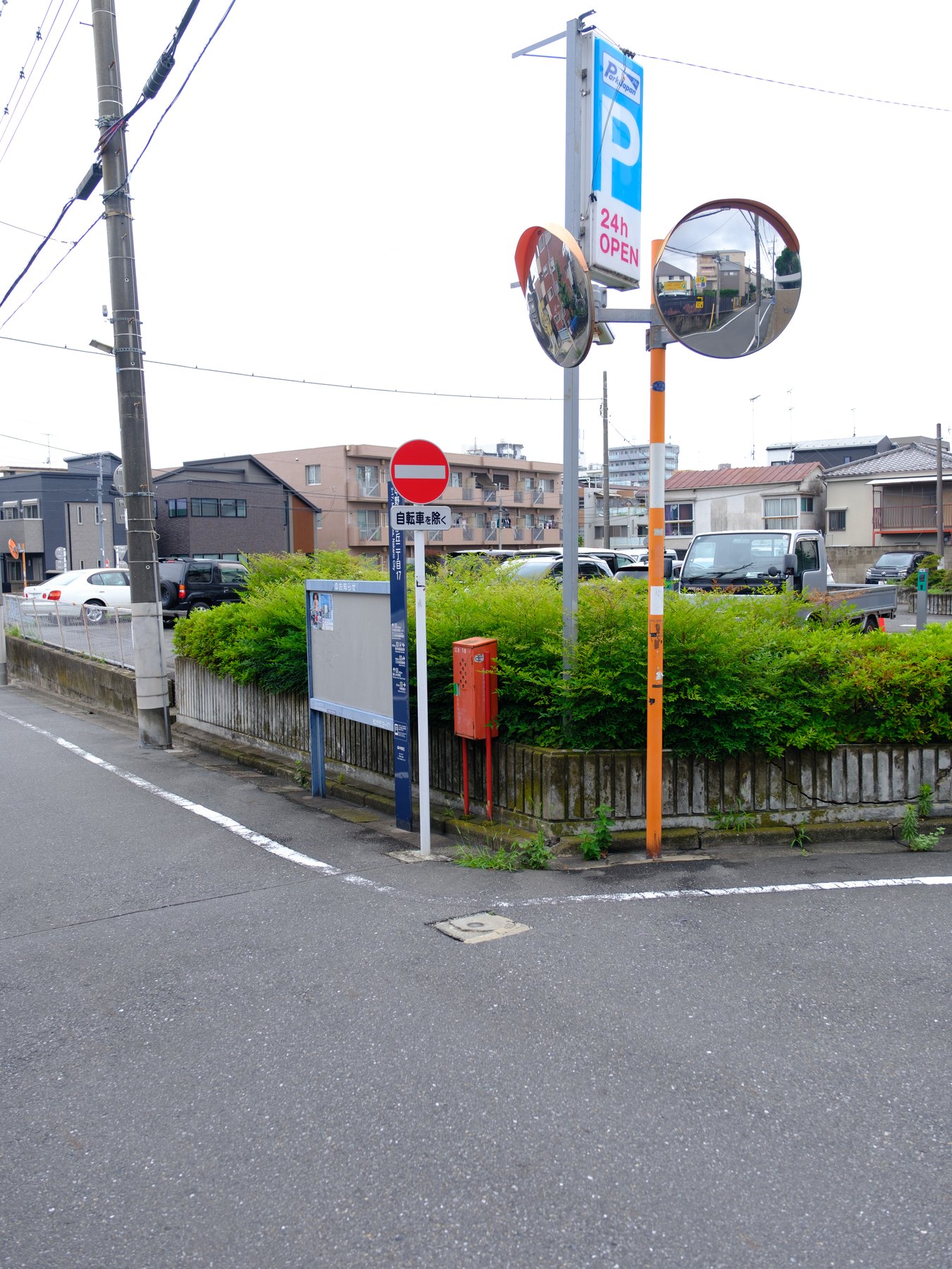 An ordinary Tokyo street corner layered with mirrors, signs, plants, utility lines, and neighborhood buildings